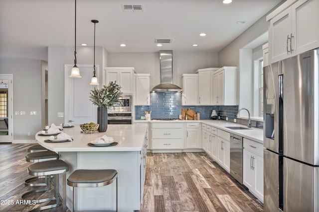 kitchen with white cabinets, sink, wall chimney exhaust hood, decorative light fixtures, and stainless steel appliances