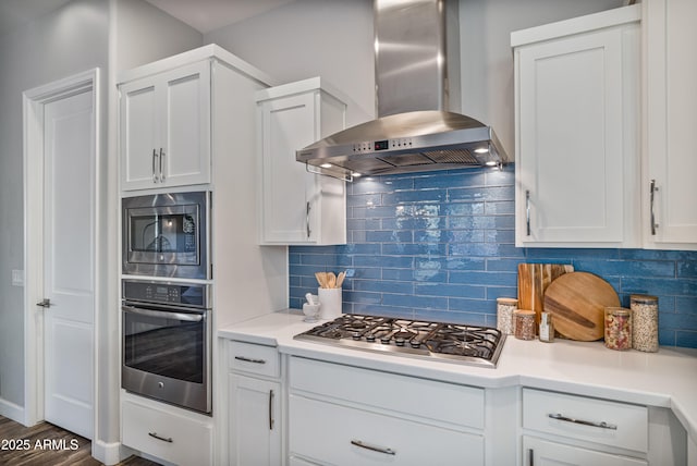 kitchen with dark hardwood / wood-style flooring, tasteful backsplash, wall chimney exhaust hood, stainless steel appliances, and white cabinetry