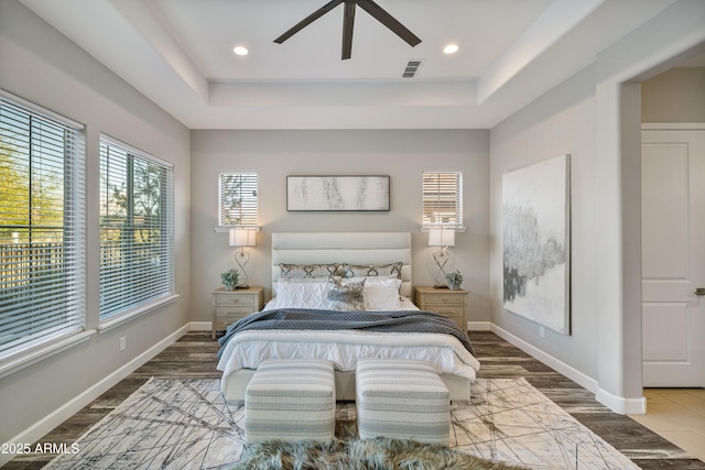 bedroom with hardwood / wood-style flooring, ceiling fan, and a raised ceiling