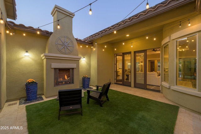 patio terrace at dusk with a yard and exterior fireplace