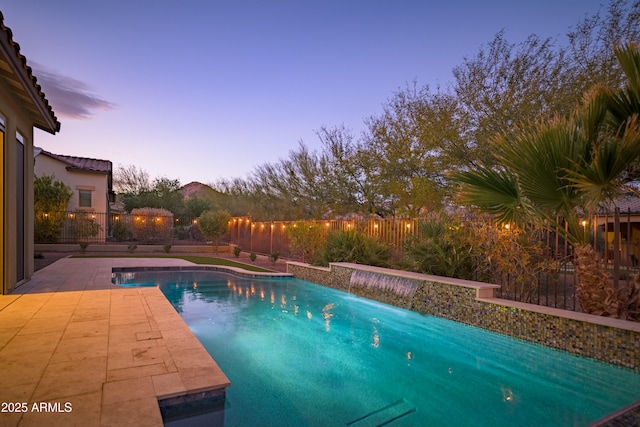 pool at dusk featuring pool water feature and a patio