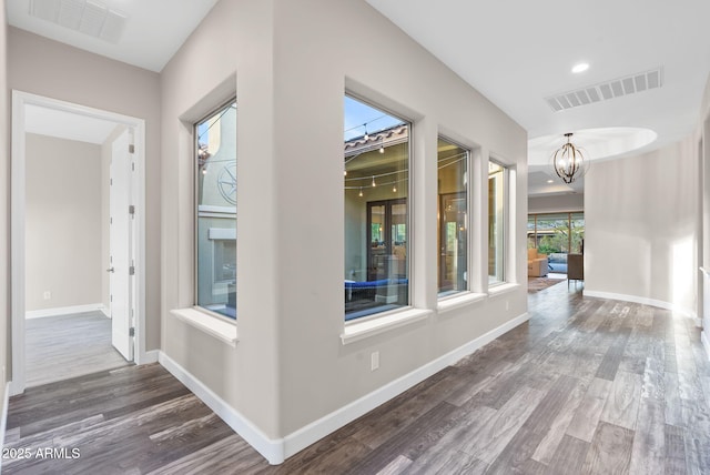 hallway with a wealth of natural light, dark hardwood / wood-style floors, and a notable chandelier