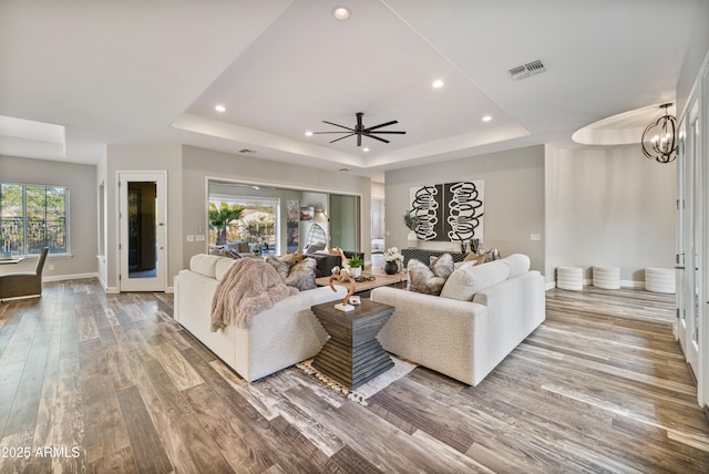 living room featuring ceiling fan with notable chandelier, light wood-type flooring, and a tray ceiling