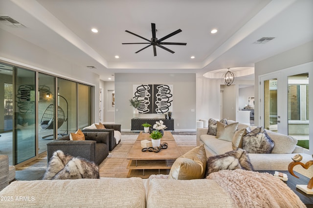 living room with ceiling fan with notable chandelier, light wood-type flooring, a tray ceiling, and french doors