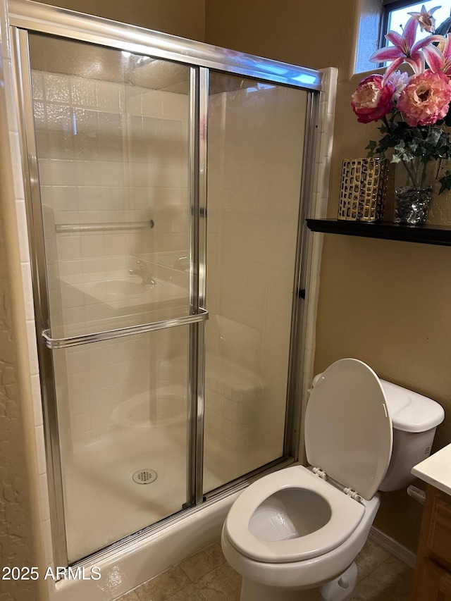 bathroom with a shower with door, vanity, tile patterned floors, and toilet