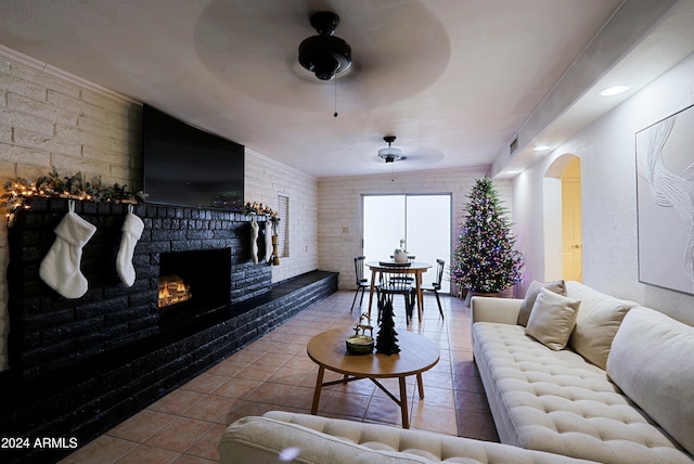 living room featuring a fireplace, ceiling fan, tile patterned flooring, and brick wall