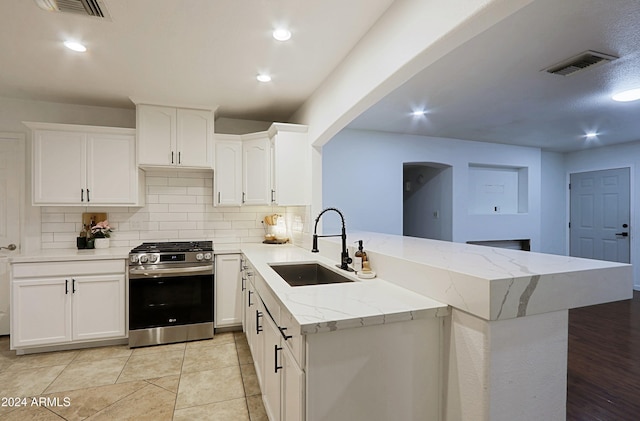 kitchen featuring kitchen peninsula, sink, decorative backsplash, stainless steel range oven, and white cabinetry