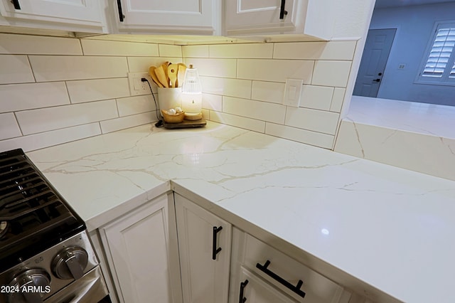 kitchen with backsplash, light stone counters, stainless steel range, and white cabinets