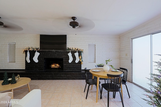 dining space with ceiling fan, light tile patterned flooring, brick wall, and a brick fireplace