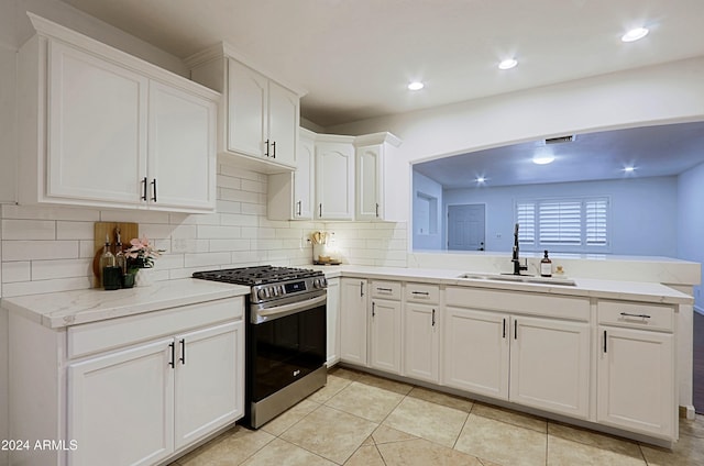 kitchen with kitchen peninsula, gas range, sink, light tile patterned floors, and white cabinetry