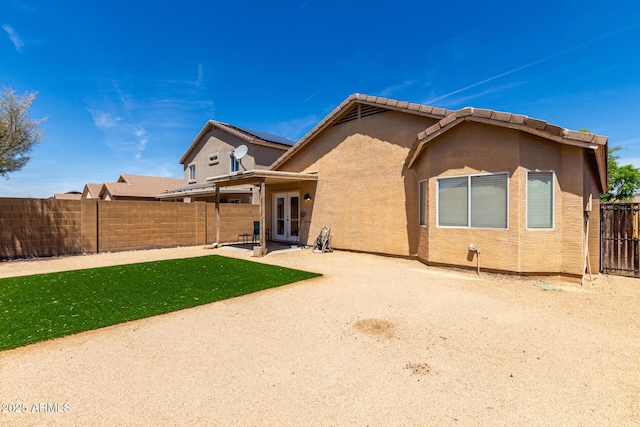 rear view of house with french doors, a lawn, a fenced backyard, a patio, and stucco siding
