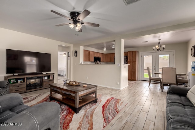 living area featuring baseboards, light wood-style flooring, ceiling fan with notable chandelier, and visible vents