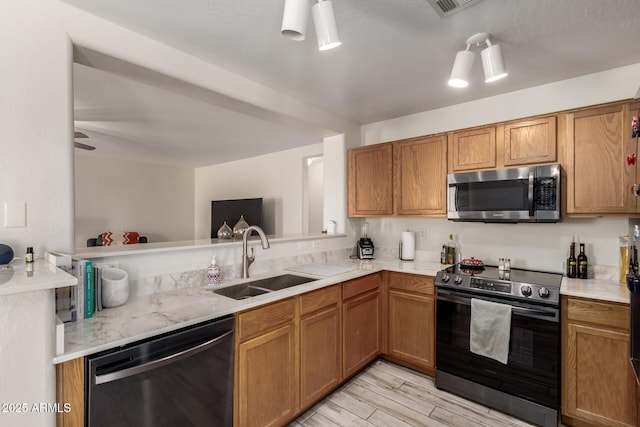 kitchen featuring brown cabinets, a sink, light wood finished floors, light countertops, and stainless steel appliances