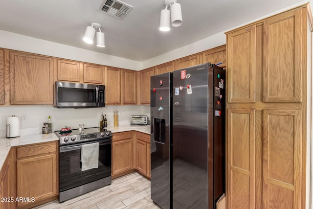 kitchen featuring brown cabinetry, visible vents, appliances with stainless steel finishes, light wood-type flooring, and light countertops