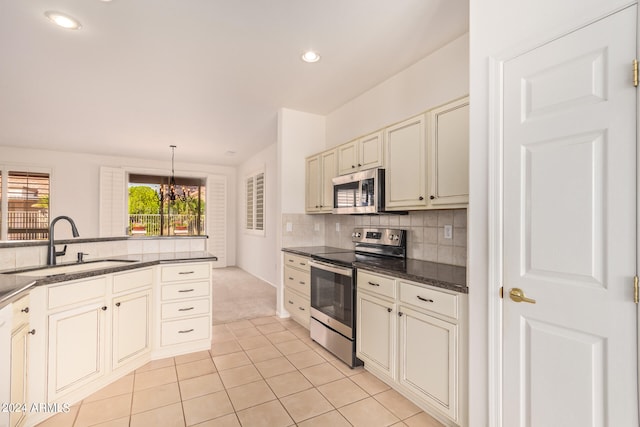 kitchen with appliances with stainless steel finishes, sink, light tile patterned floors, cream cabinets, and decorative light fixtures