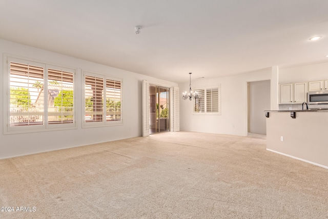 unfurnished living room with light carpet, sink, and a notable chandelier