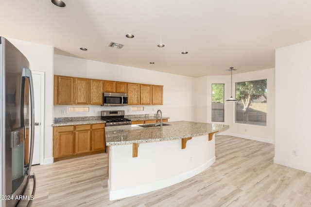 kitchen featuring a center island with sink, light wood-type flooring, hanging light fixtures, and stainless steel appliances