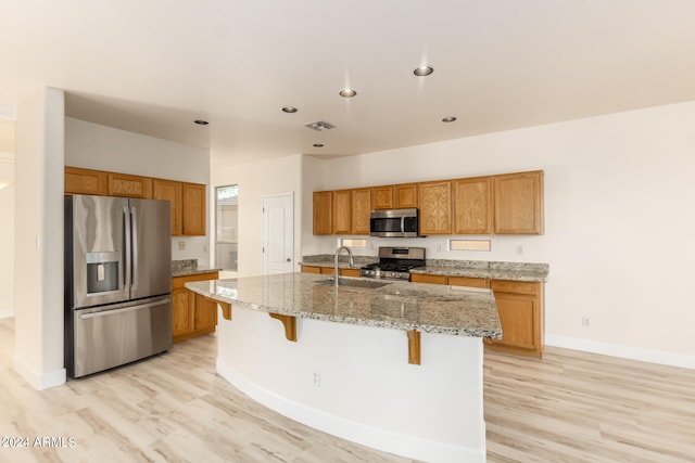 kitchen featuring a center island with sink, light hardwood / wood-style floors, appliances with stainless steel finishes, and a kitchen breakfast bar