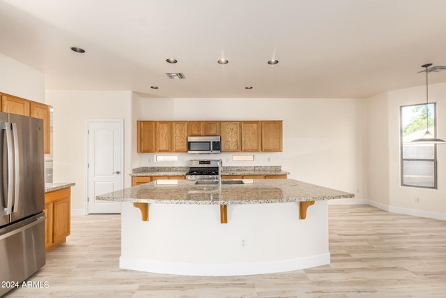 kitchen featuring stainless steel appliances, a center island with sink, light wood-type flooring, and a breakfast bar