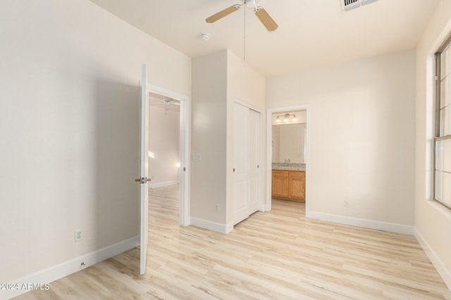 unfurnished bedroom with a closet, ensuite bath, light wood-type flooring, and ceiling fan