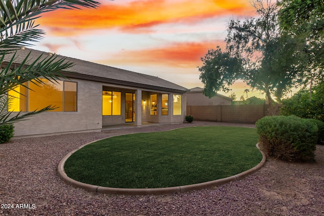 back house at dusk featuring a lawn