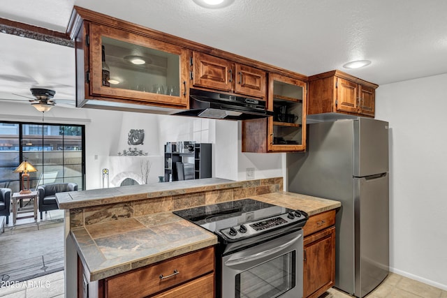 kitchen featuring ceiling fan, exhaust hood, kitchen peninsula, appliances with stainless steel finishes, and a textured ceiling