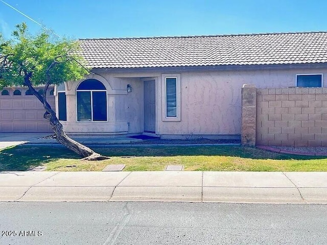 view of front of property with stucco siding, a tile roof, fence, and a garage