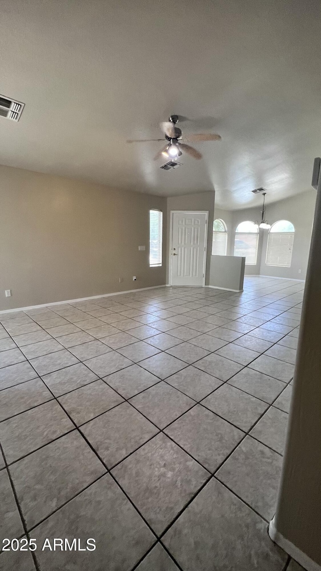 empty room featuring ceiling fan with notable chandelier, visible vents, a wealth of natural light, and light tile patterned flooring
