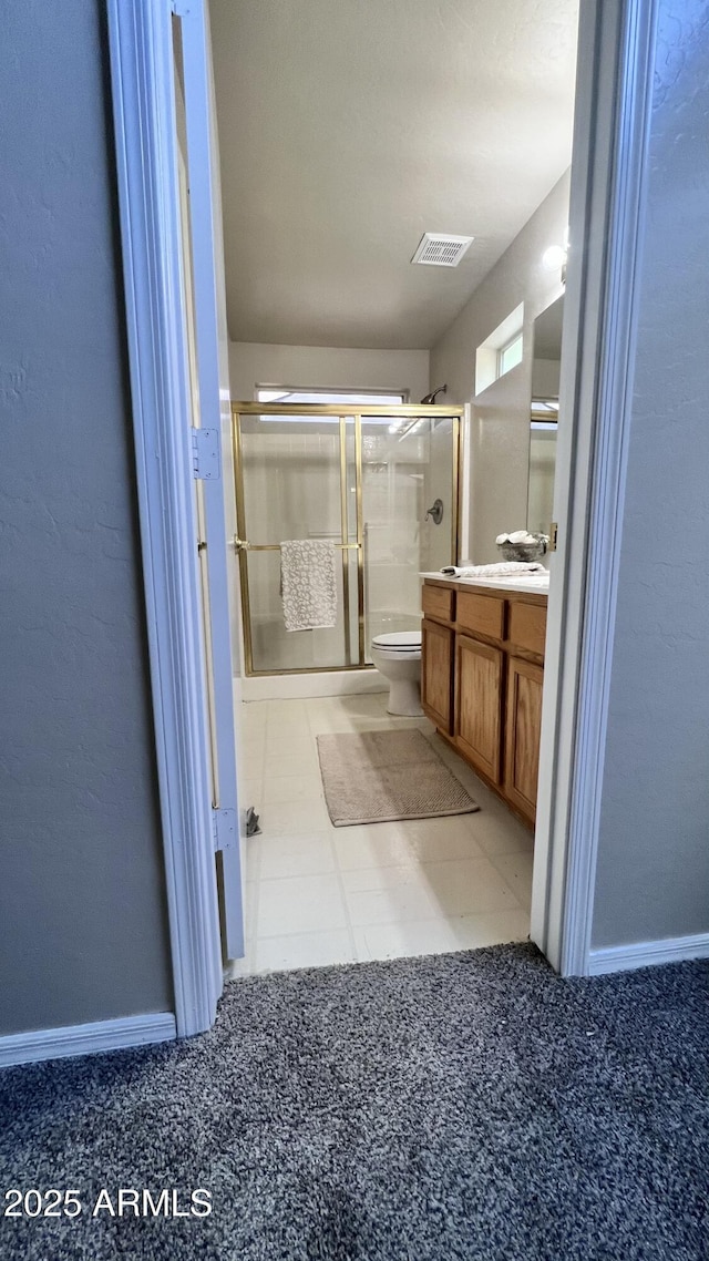 bathroom with a shower with shower door, visible vents, toilet, vanity, and baseboards