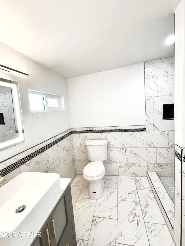 bathroom with walk in shower, vanity, toilet, and tile walls