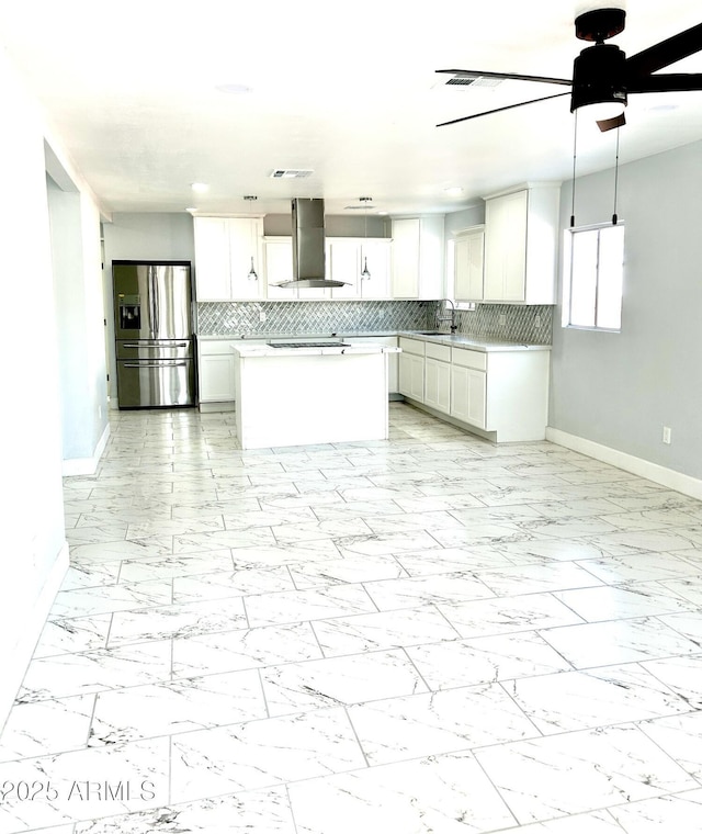 kitchen featuring stainless steel refrigerator with ice dispenser, tasteful backsplash, ceiling fan, wall chimney range hood, and white cabinetry