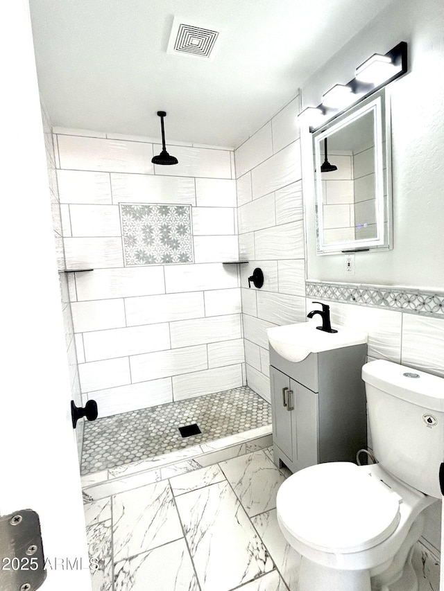 bathroom with tiled shower, vanity, toilet, and tile walls