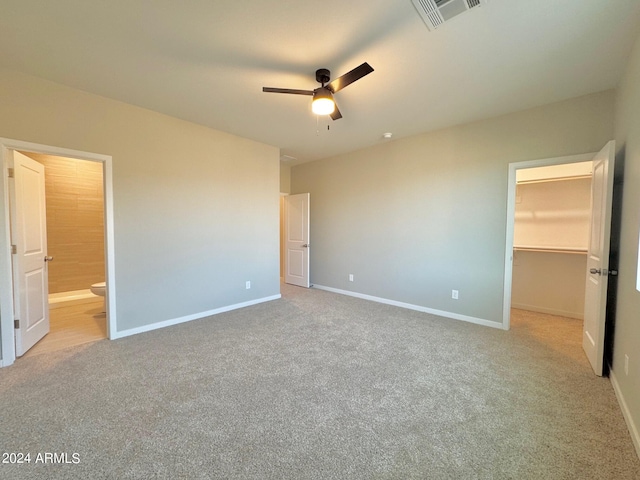 unfurnished bedroom with a walk in closet, ensuite bath, a closet, ceiling fan, and light colored carpet