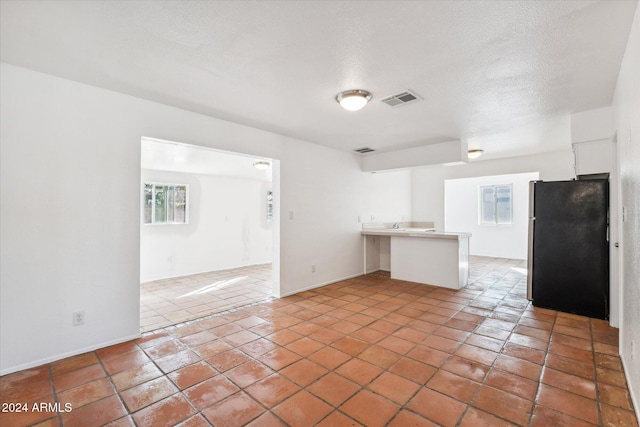 kitchen featuring kitchen peninsula, a textured ceiling, white cabinetry, fridge, and light tile patterned flooring