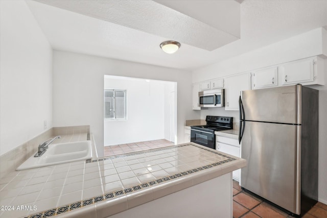 kitchen with white cabinetry, tile patterned flooring, tile countertops, a textured ceiling, and appliances with stainless steel finishes