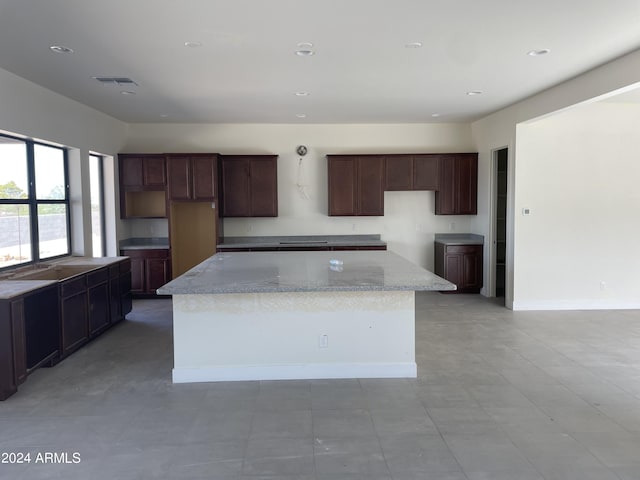 kitchen with dark brown cabinets, light stone countertops, a center island, and light tile patterned floors