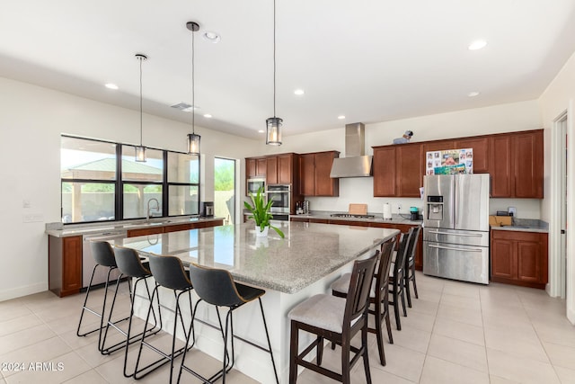 kitchen featuring a large island, hanging light fixtures, appliances with stainless steel finishes, wall chimney exhaust hood, and light stone counters