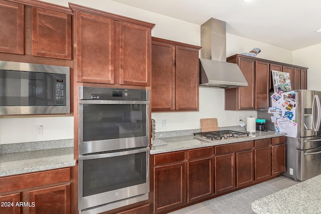 kitchen with light stone countertops, wall chimney range hood, stainless steel appliances, and light tile patterned floors