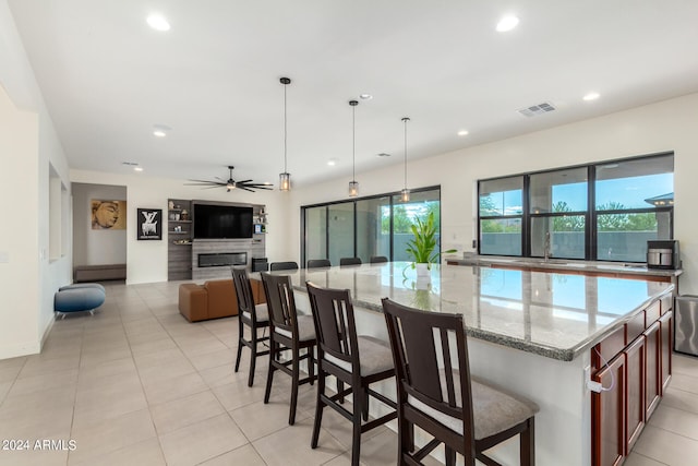 kitchen featuring light tile patterned flooring, a kitchen breakfast bar, hanging light fixtures, ceiling fan, and light stone counters