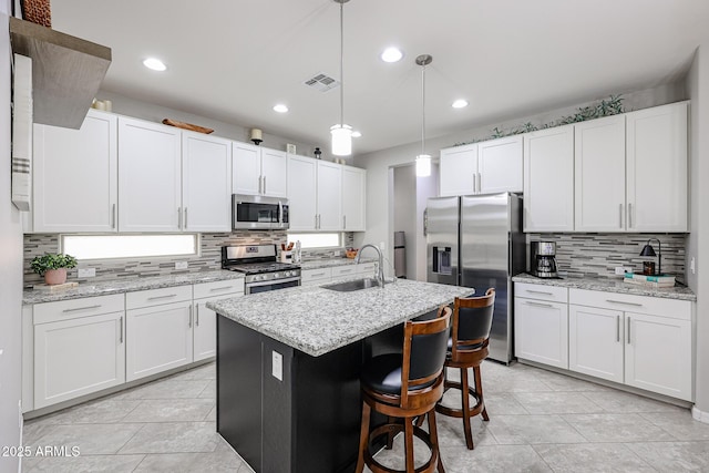 kitchen featuring decorative light fixtures, an island with sink, sink, white cabinets, and stainless steel appliances