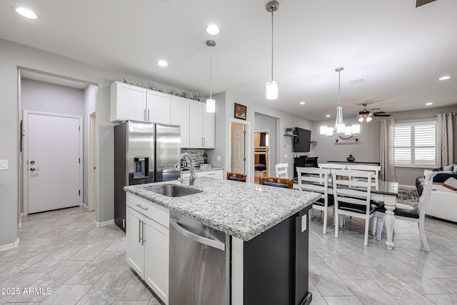 kitchen featuring stainless steel appliances, a kitchen island with sink, pendant lighting, and white cabinets