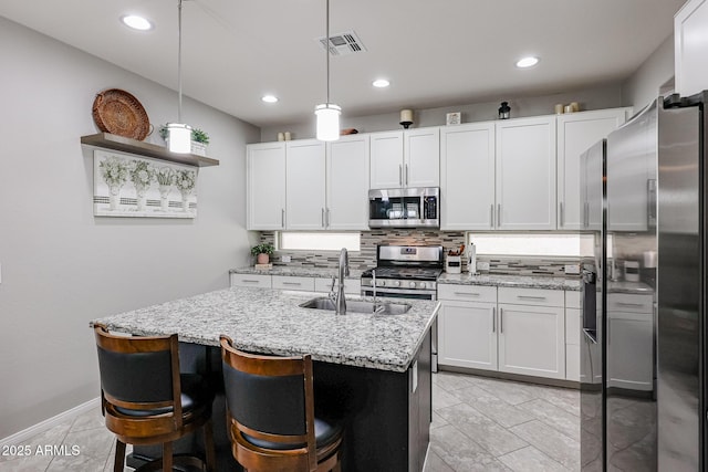 kitchen featuring sink, decorative light fixtures, stainless steel appliances, a kitchen island with sink, and white cabinets