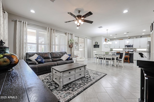 tiled living room featuring ceiling fan with notable chandelier