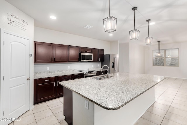 kitchen featuring a center island with sink, a sink, stainless steel appliances, light tile patterned floors, and dark brown cabinets