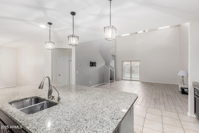 kitchen featuring light stone countertops, light wood-style flooring, a sink, hanging light fixtures, and open floor plan