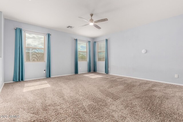 carpeted empty room featuring plenty of natural light, a ceiling fan, visible vents, and baseboards