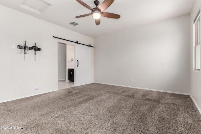 carpeted spare room with visible vents, a ceiling fan, a barn door, baseboards, and attic access