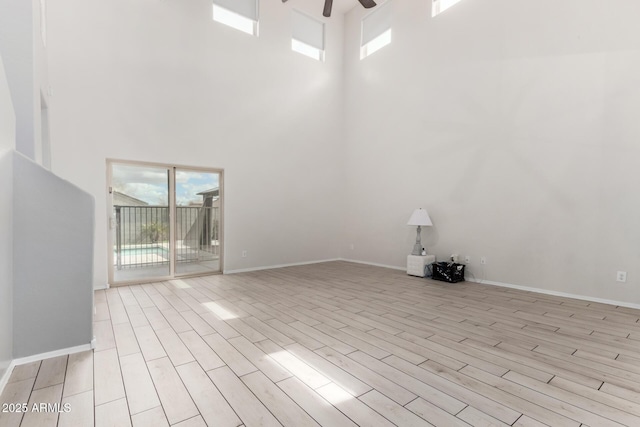 empty room featuring ceiling fan, baseboards, light wood-style floors, and a towering ceiling