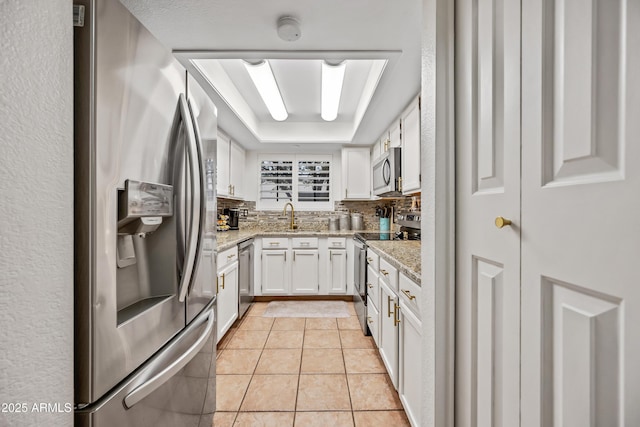 kitchen with a sink, backsplash, appliances with stainless steel finishes, white cabinets, and light tile patterned floors