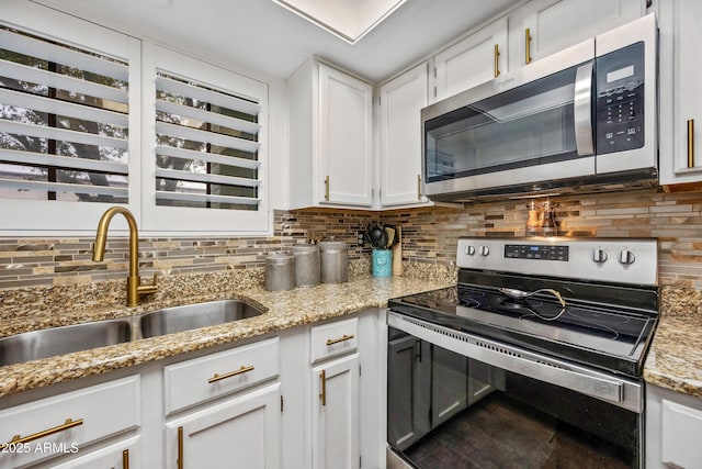 kitchen featuring a sink, appliances with stainless steel finishes, white cabinets, decorative backsplash, and light stone countertops